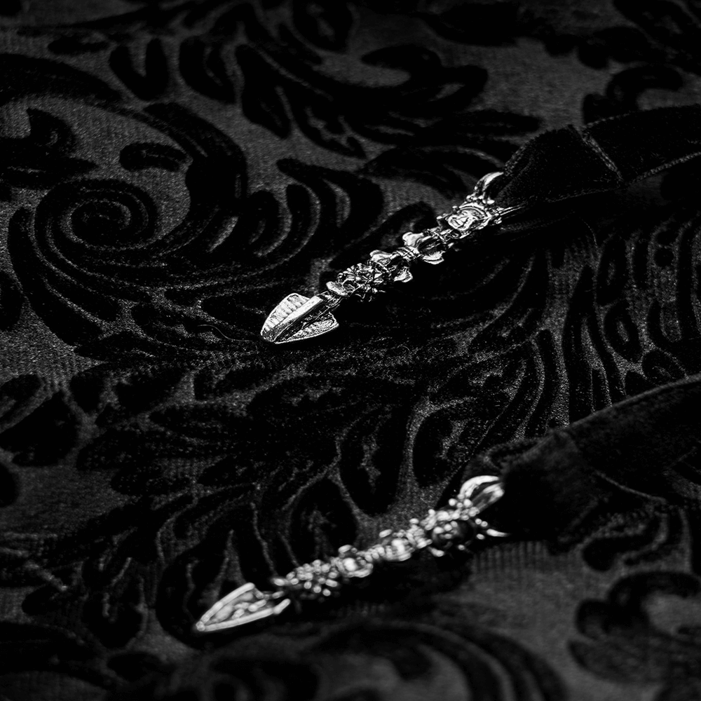 Close-up of ornate silver clasps on black gothic velvet fabric with intricate floral patterns.