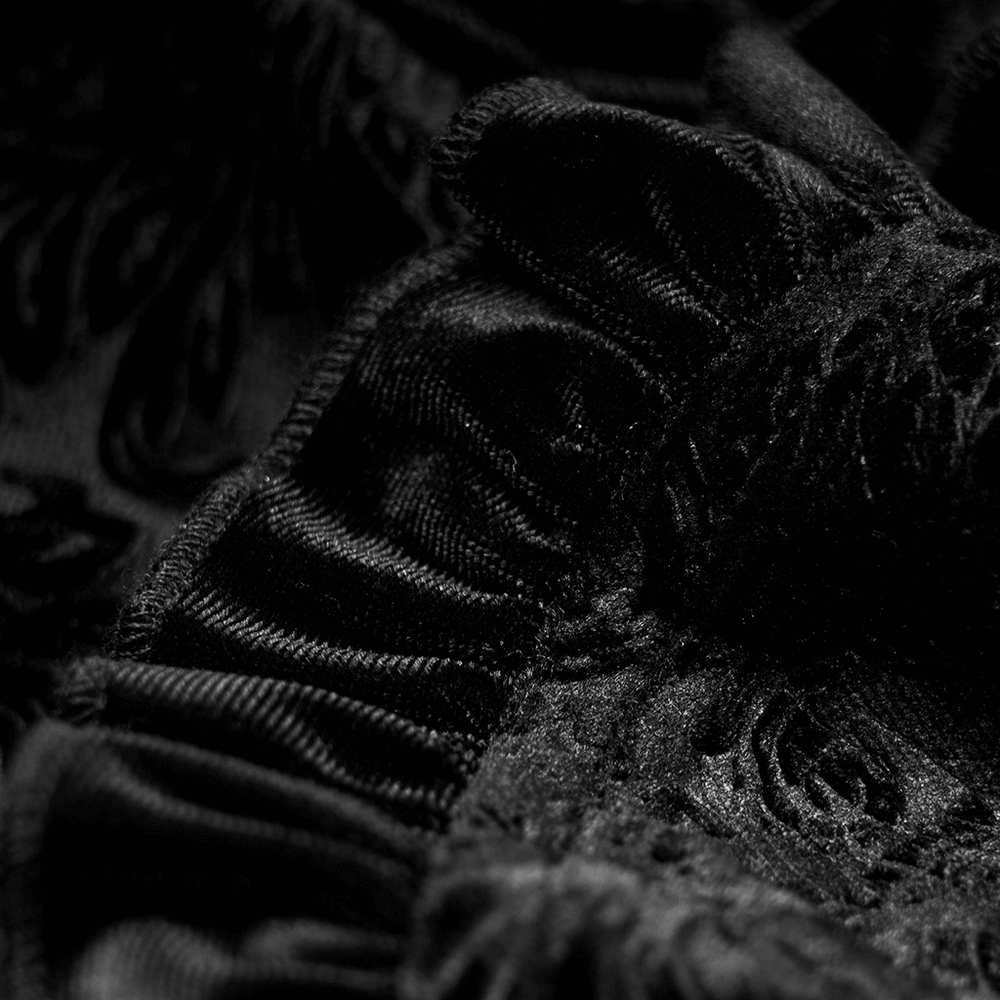 Close-up of luxurious black gothic velvet fabric with intricate shadow flower patterns and delicate ruffles.