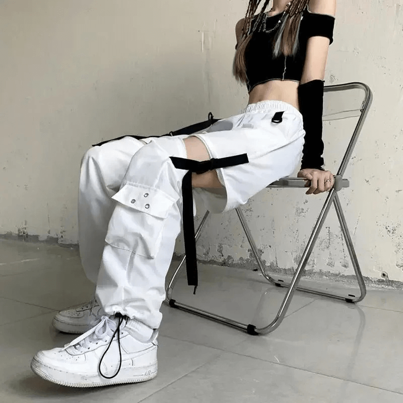 Model showcasing trendy white cargo pants with cutouts and buckles, paired with a stylish crop top and sneakers.