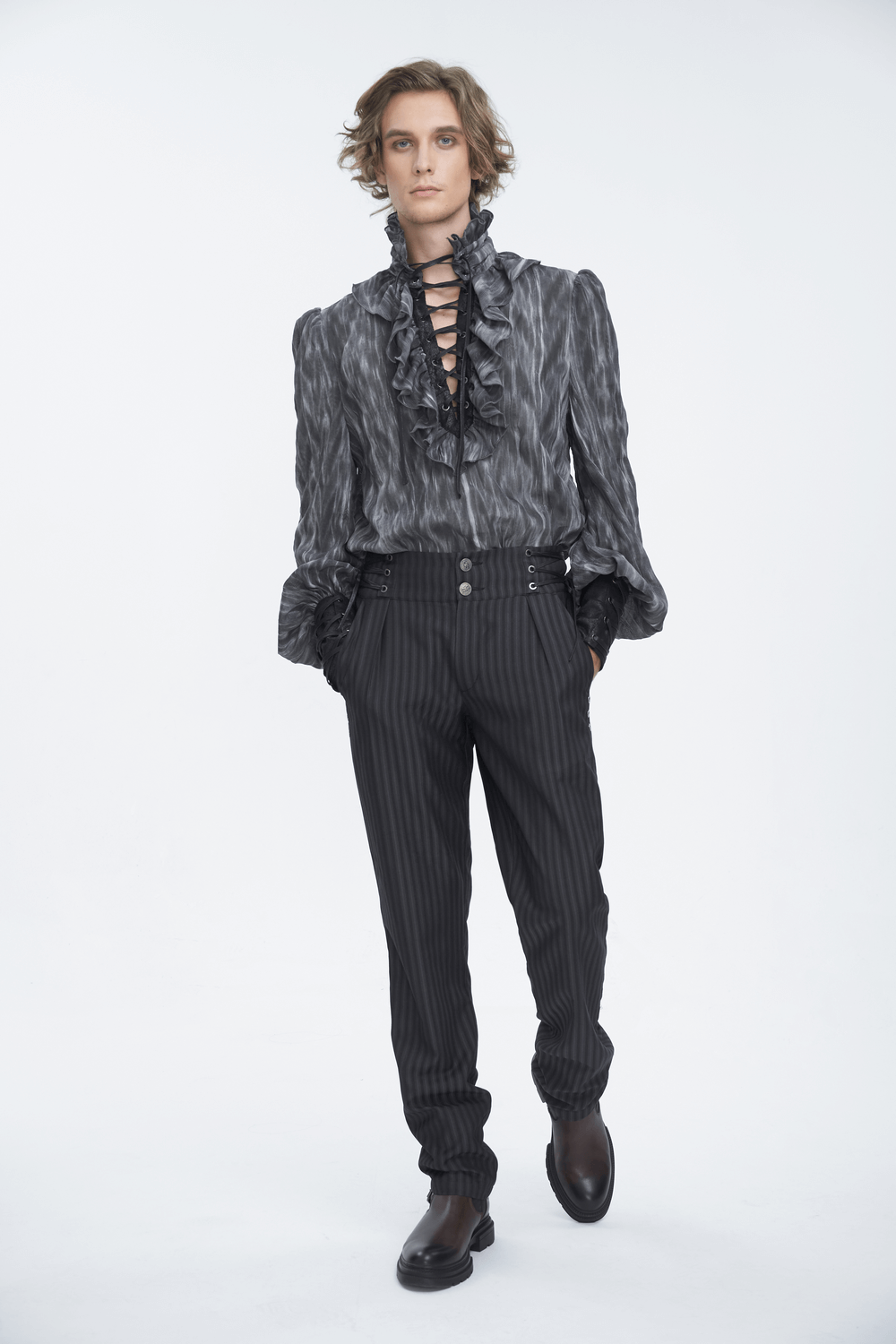 Stylish man in a ruffled black and grey blouse with lace-up detail, paired with striped trousers, exuding edgy fashion.