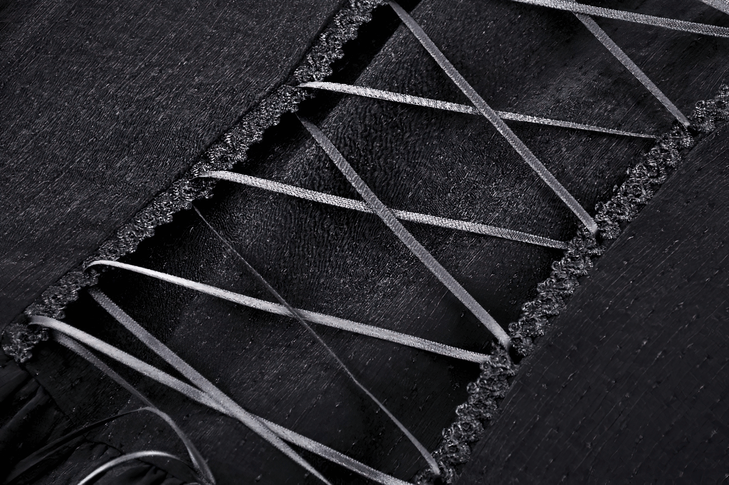 Close-up of corset lace-up detail on a black dress, showcasing elegant ribbons and intricate lace trim.