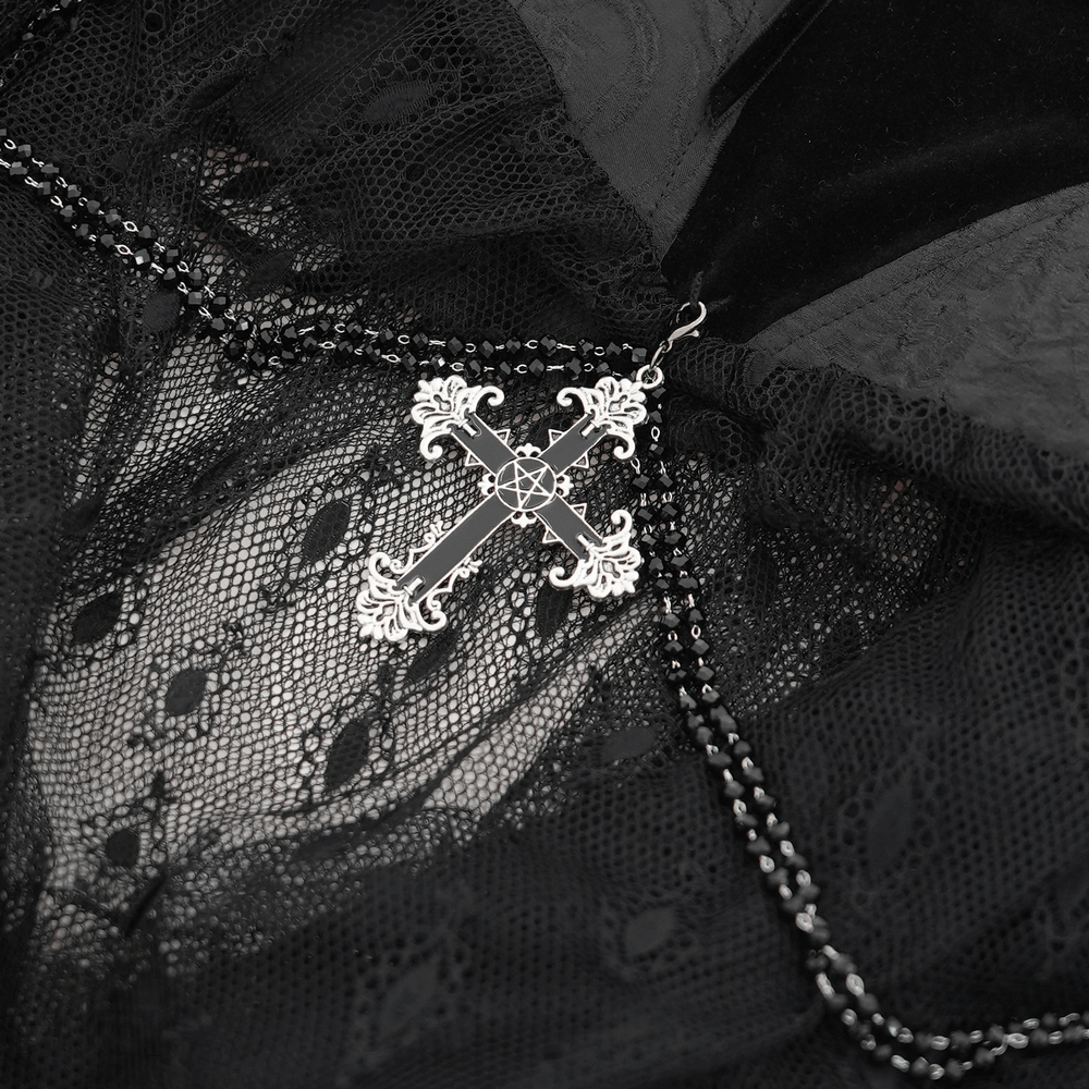 Close-up of an intricate silver cross pendant on black lace featuring chains, perfect for gothic fashion enthusiasts.