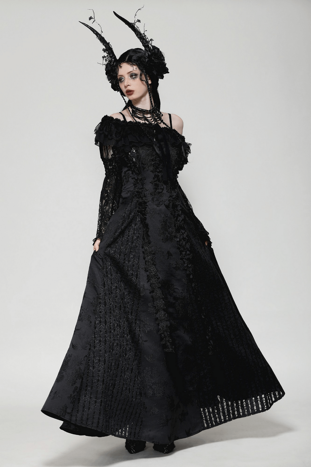 Elegant model in a black lace gothic off-shoulder cape dress with dramatic bell sleeves and intricate floral details.