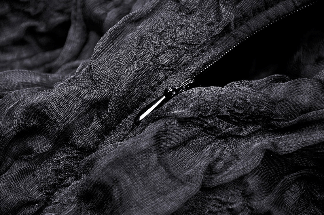 Close-up of intricate black lace fabric and zipper detailing on a flowy high-low dress.