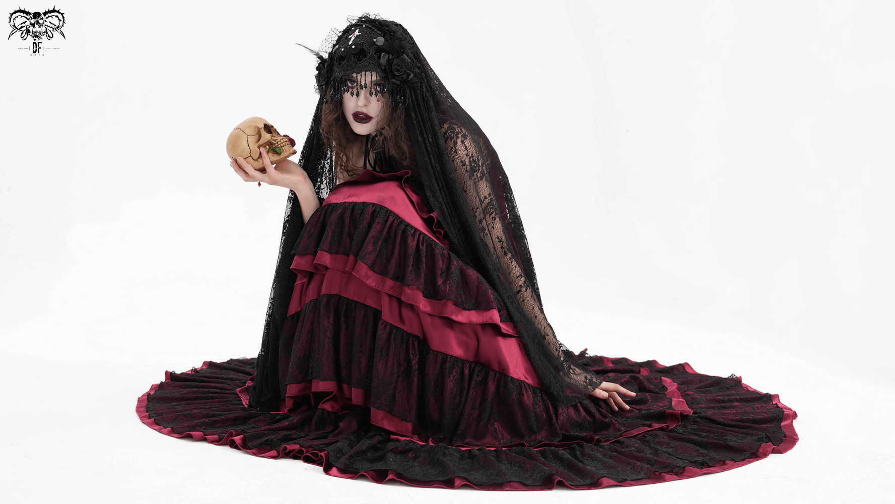 Gothic woman in a black lace veil and red dress holding a skull, embodying dark elegance and mystique.