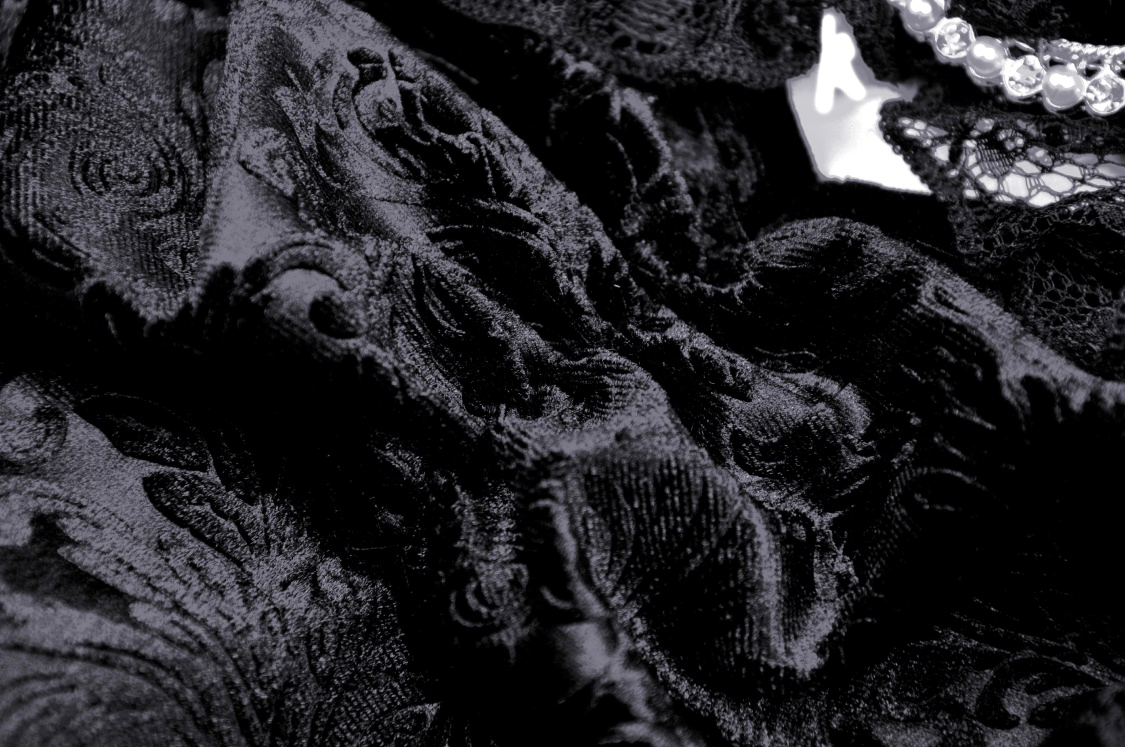 Close-up of luxurious black velvet lace fabric with intricate patterns, perfect for a gothic-inspired outfit.