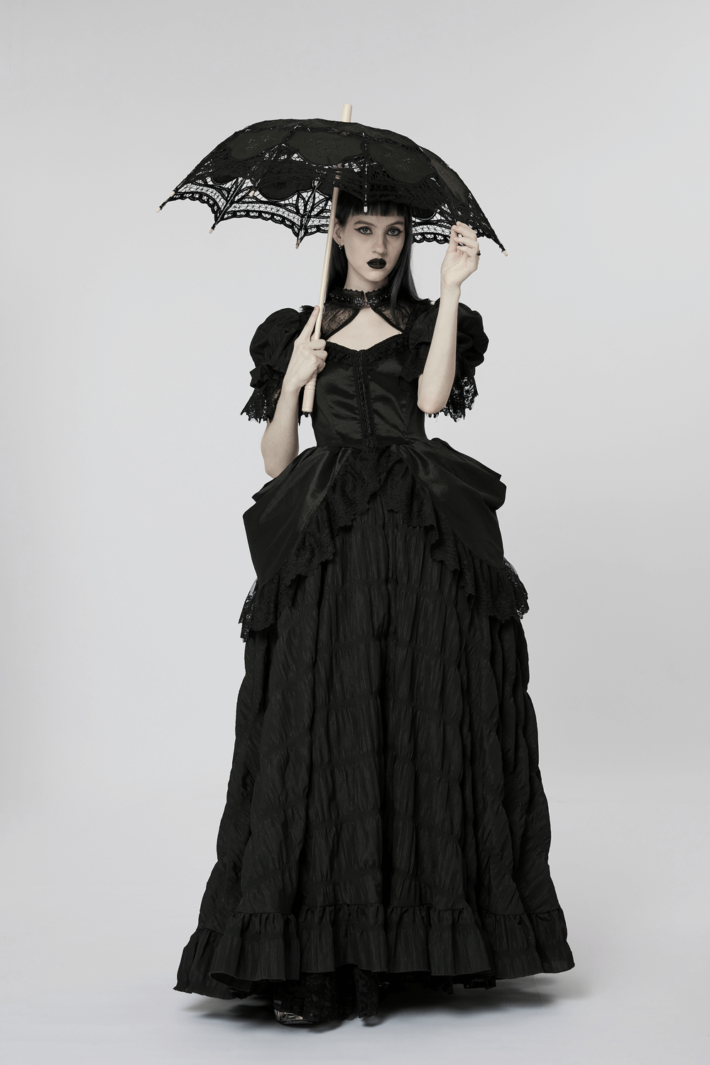 Gothic model in black dress holding a black lace parasol with embroidery, perfect for Victorian events.
