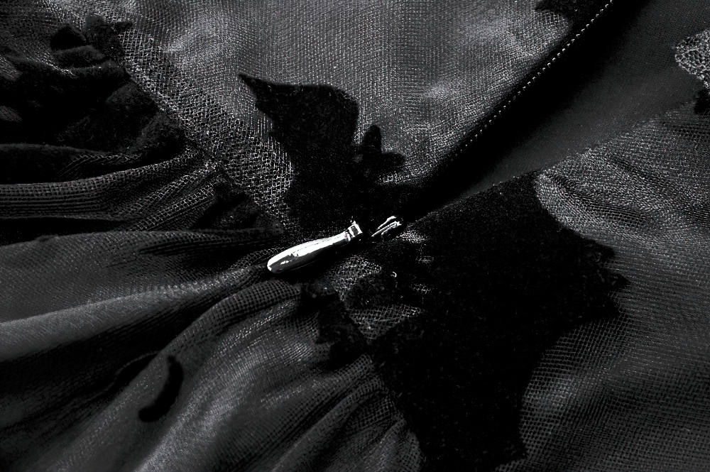 Close-up of black lace Gothic dress with bat print, showcasing ruffled layers and a delicate zipper detail.