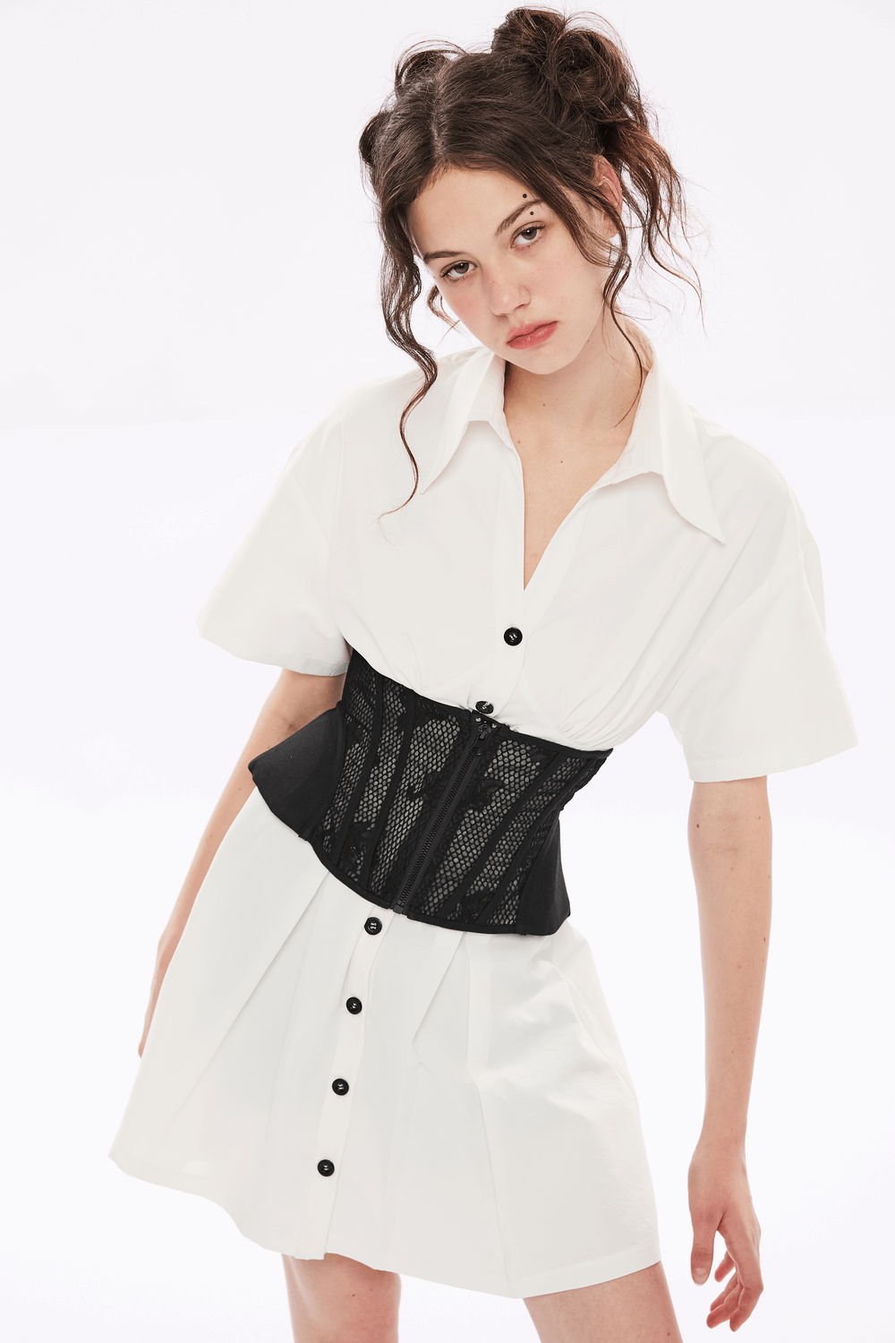Model wearing a black lace-up cincher corset with mesh panels over a white shirt dress, showcasing elegant style.