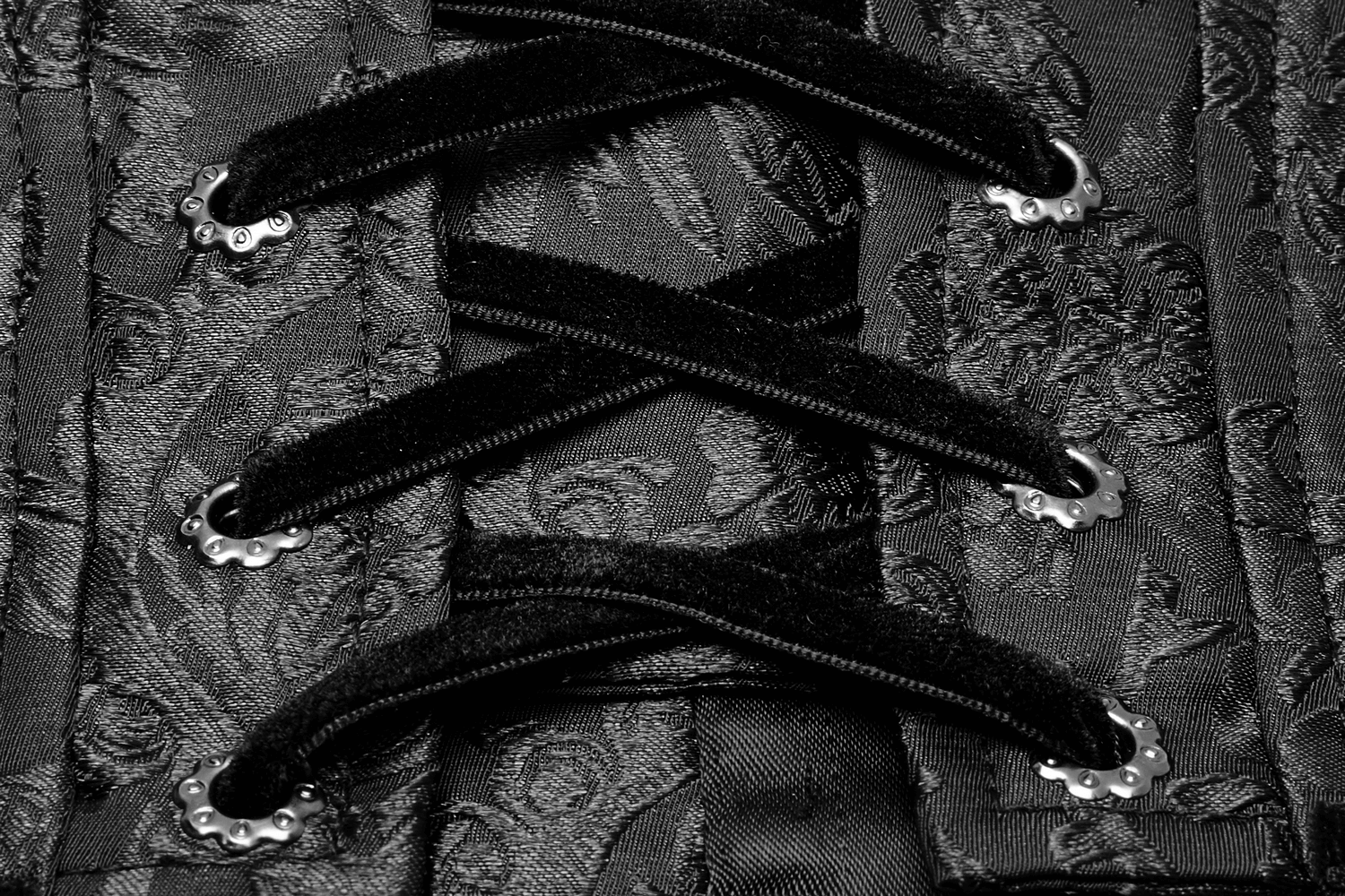 Close-up of a black lace-up corset with elegant jacquard fabric and metallic eyelets for a chic, adjustable fit.