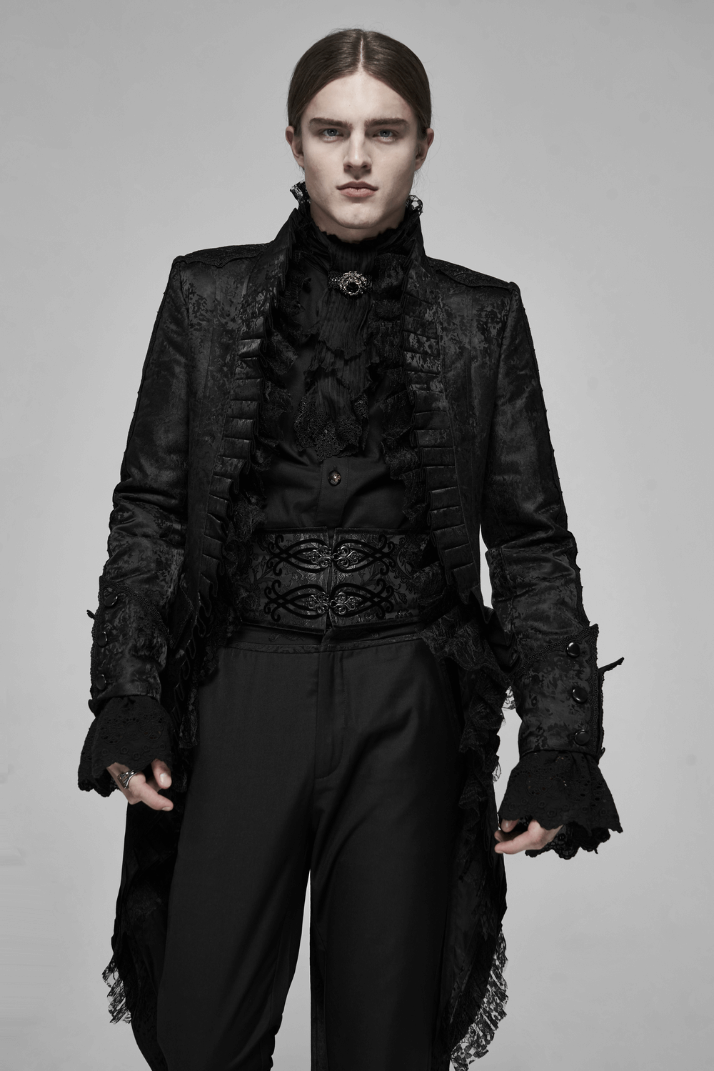 Stylish man in a black lace-up jacquard corset belt, wearing an elegant dark coat with ruffles, exuding an edgy vibe.