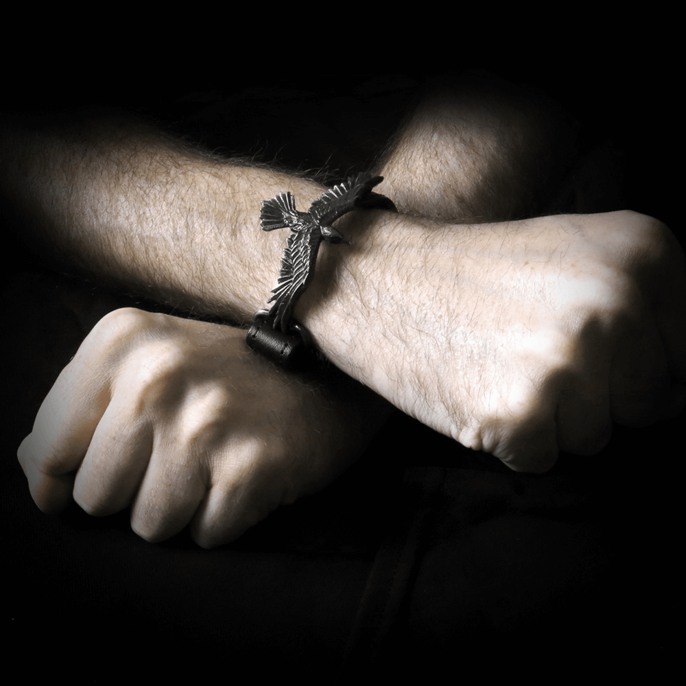Black leather wristband with pewter raven charm wrapped around a wrist, showcasing Gothic Norse mythology style.