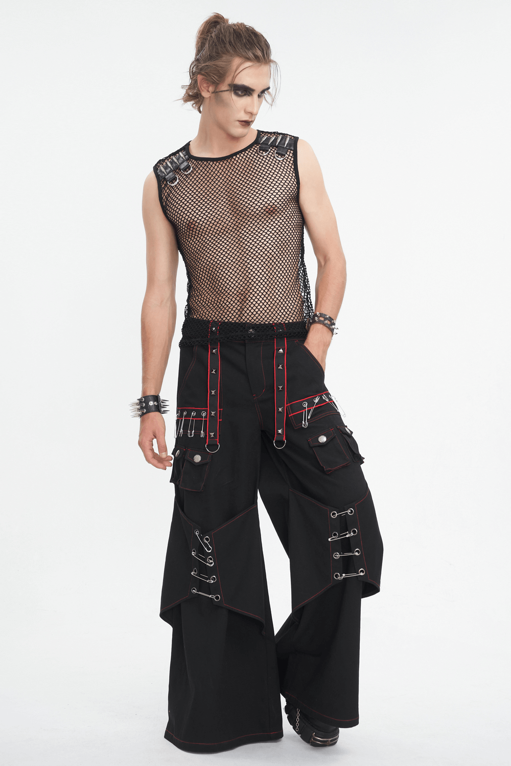 Edgy male model in black mesh tank top with spike straps and baggy cargo pants, showcasing punk rock fashion.