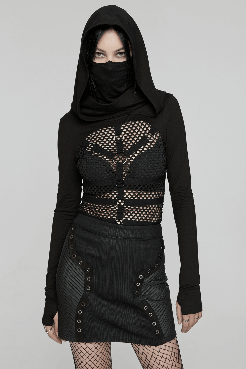 Edgy black mini skirt with rubberized leather panels, paired with a mesh crop top and hooded layer for a punk gothic style.