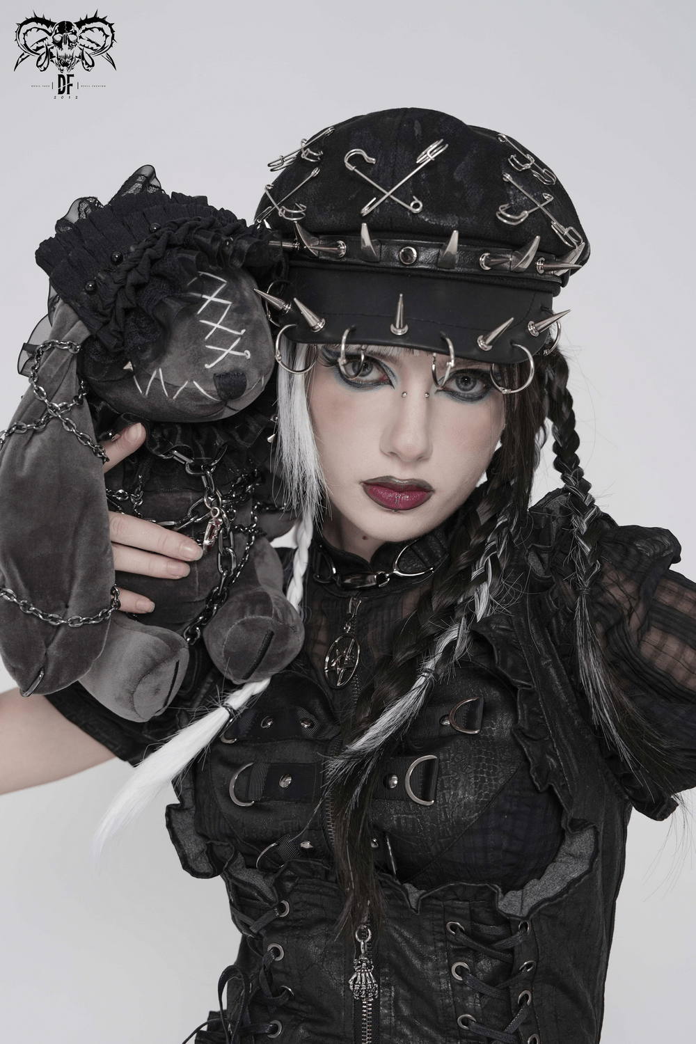 Black Punk Beret Hat with Spikes Rings and Safety Pin Trim worn by model holding plush toy, showcasing gothic and punk style.