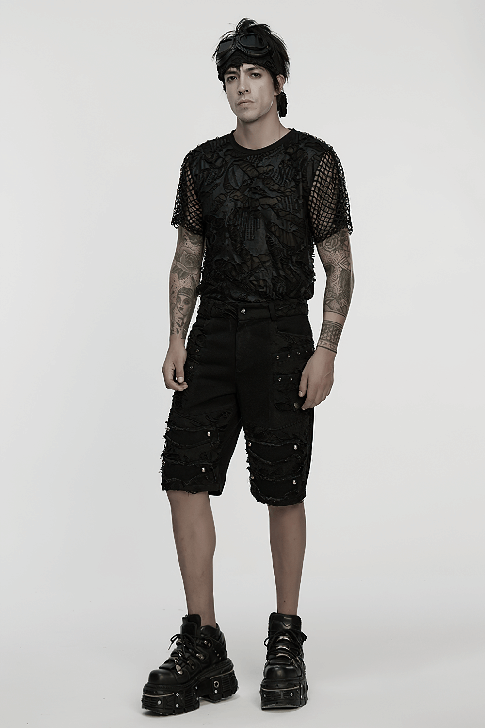 Model wearing black punk denim shorts with tattered details, tassels, and edgy footwear, showcasing alternative fashion style.