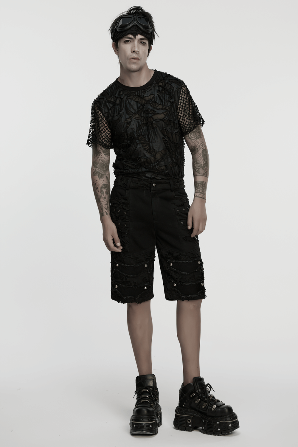 Stylish male model in black punk denim shorts with tattered details, paired with a mesh top and chunky boots.