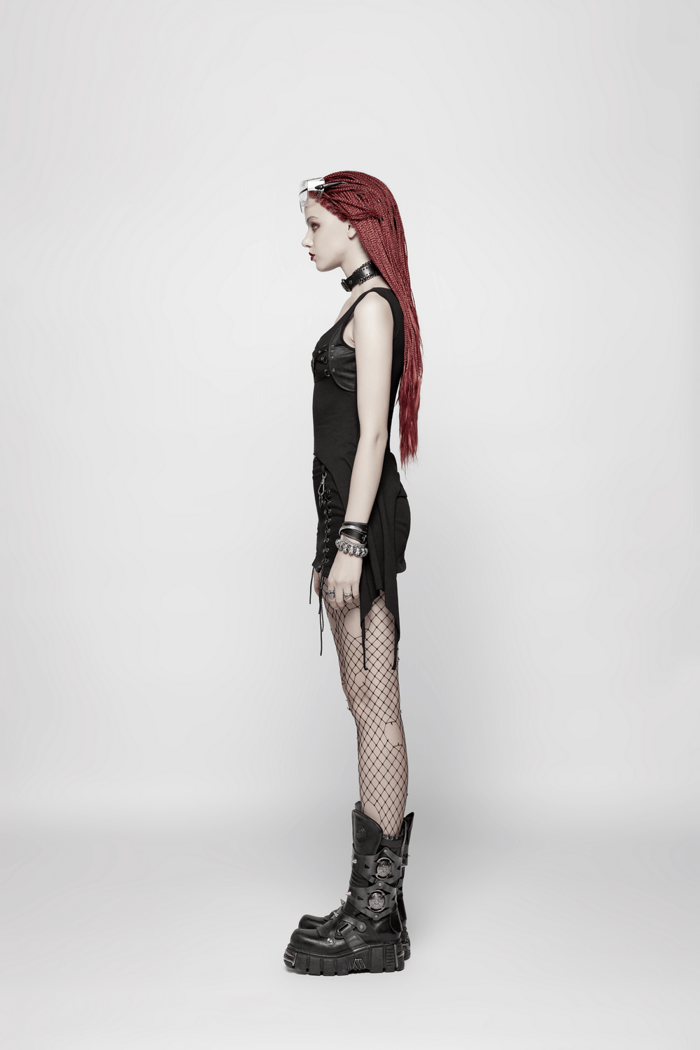 Side profile of model in black punk tank top, fishnet tights, and chunky boots showcasing edgy style.