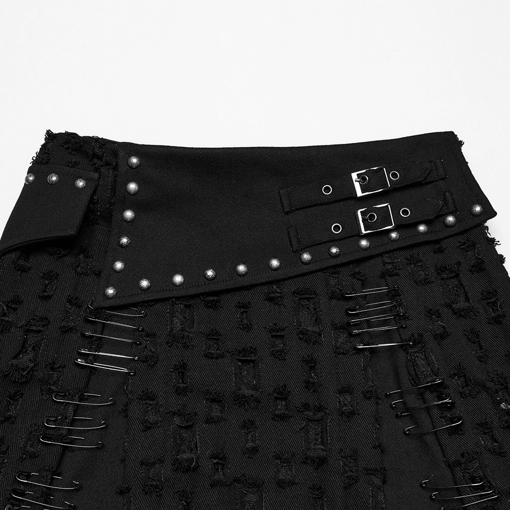 Close-up of a black punk mini skirt featuring a studded waistband and safety pin details.
