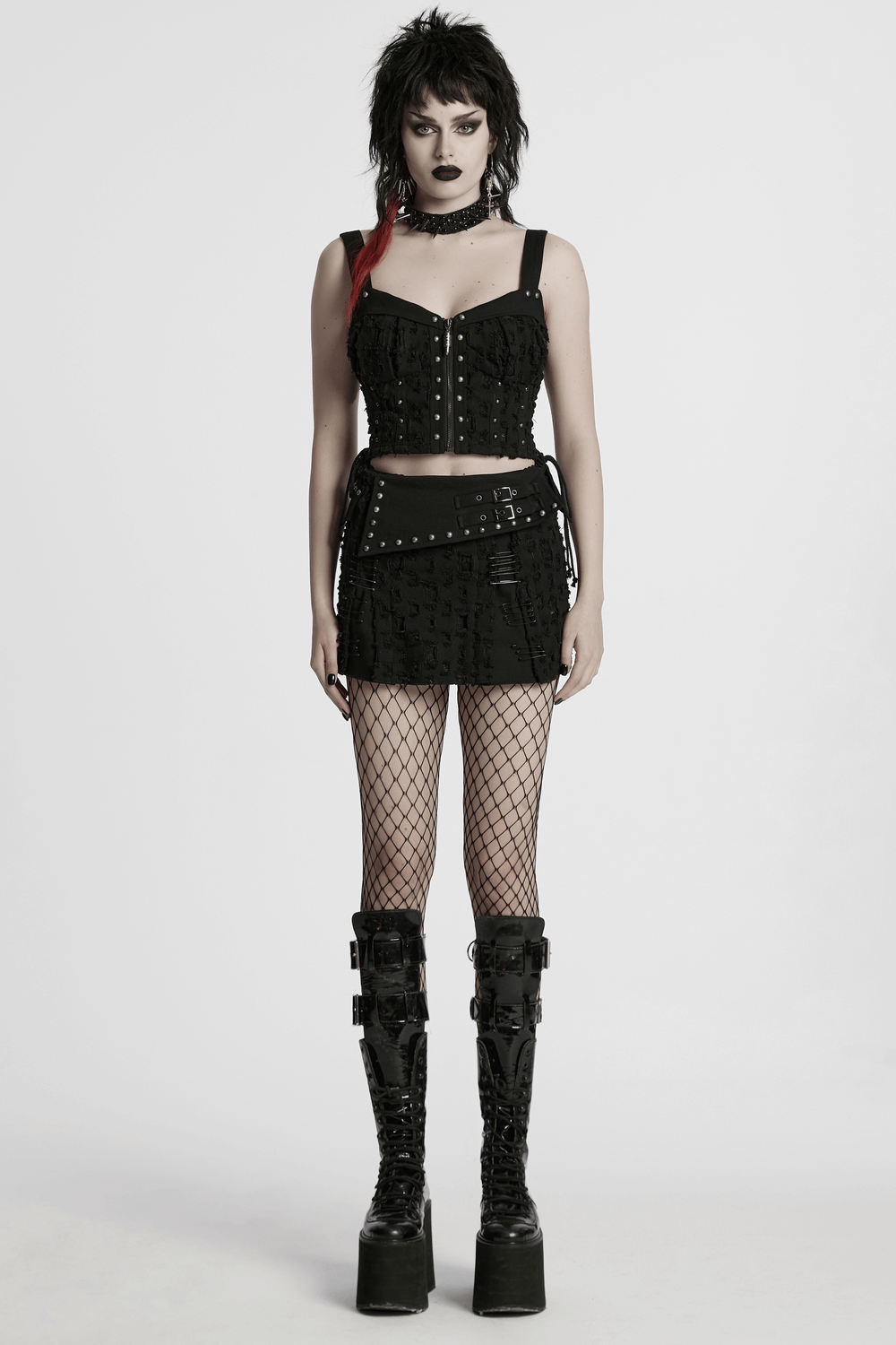 Model showcasing a black punk mini skirt with studs and safety pins, paired with a matching top and fishnet stockings.