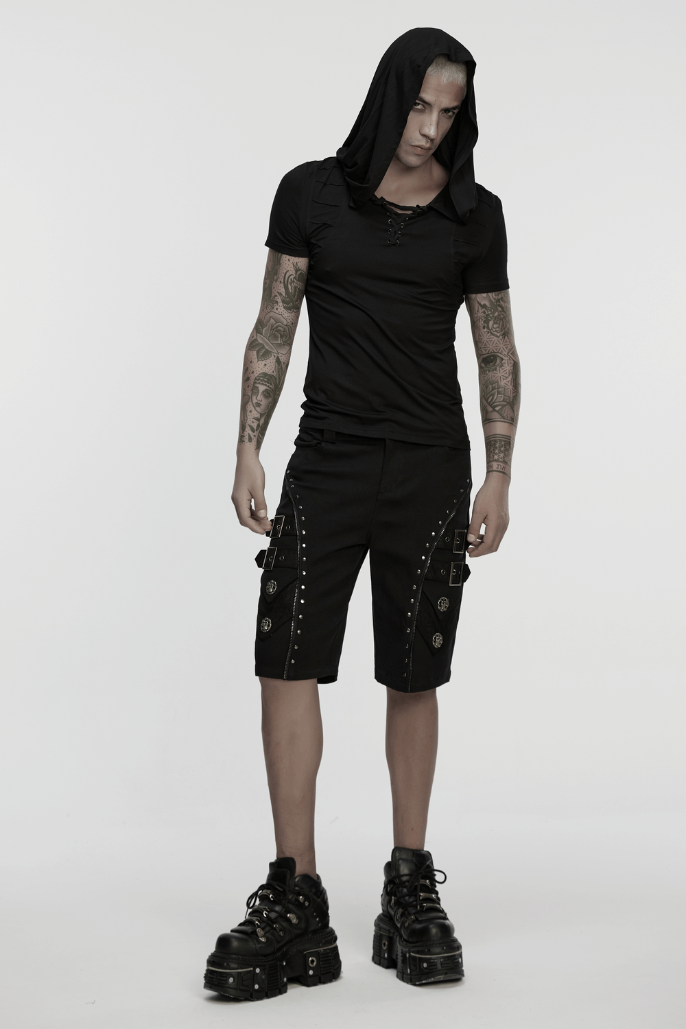 Model wearing black punk shorts with armor details and skull rivets, paired with a hooded shirt and chunky boots.