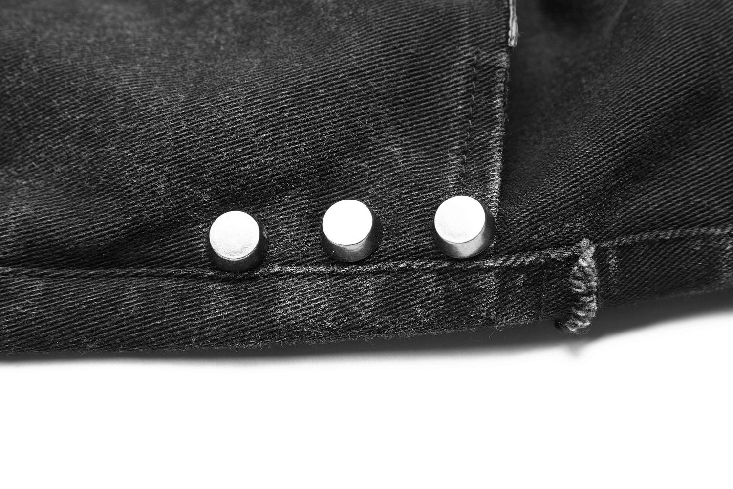 Close-up of metallic buttons on black ripped punk-style jeans with fishnet layers.