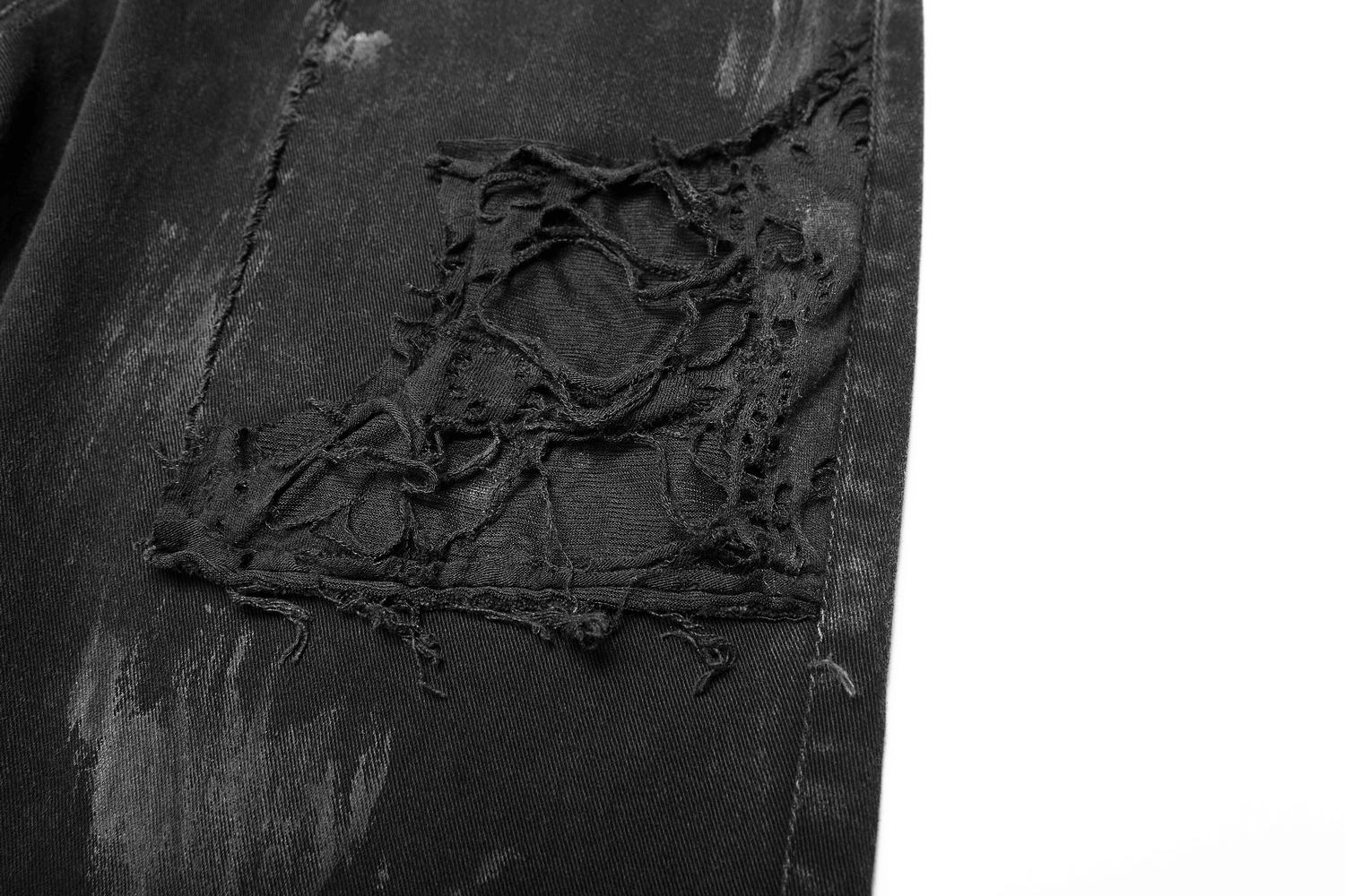 Close-up of ripped black punk-style jeans with distressed detailing and fishnet layers for a bold urban look.