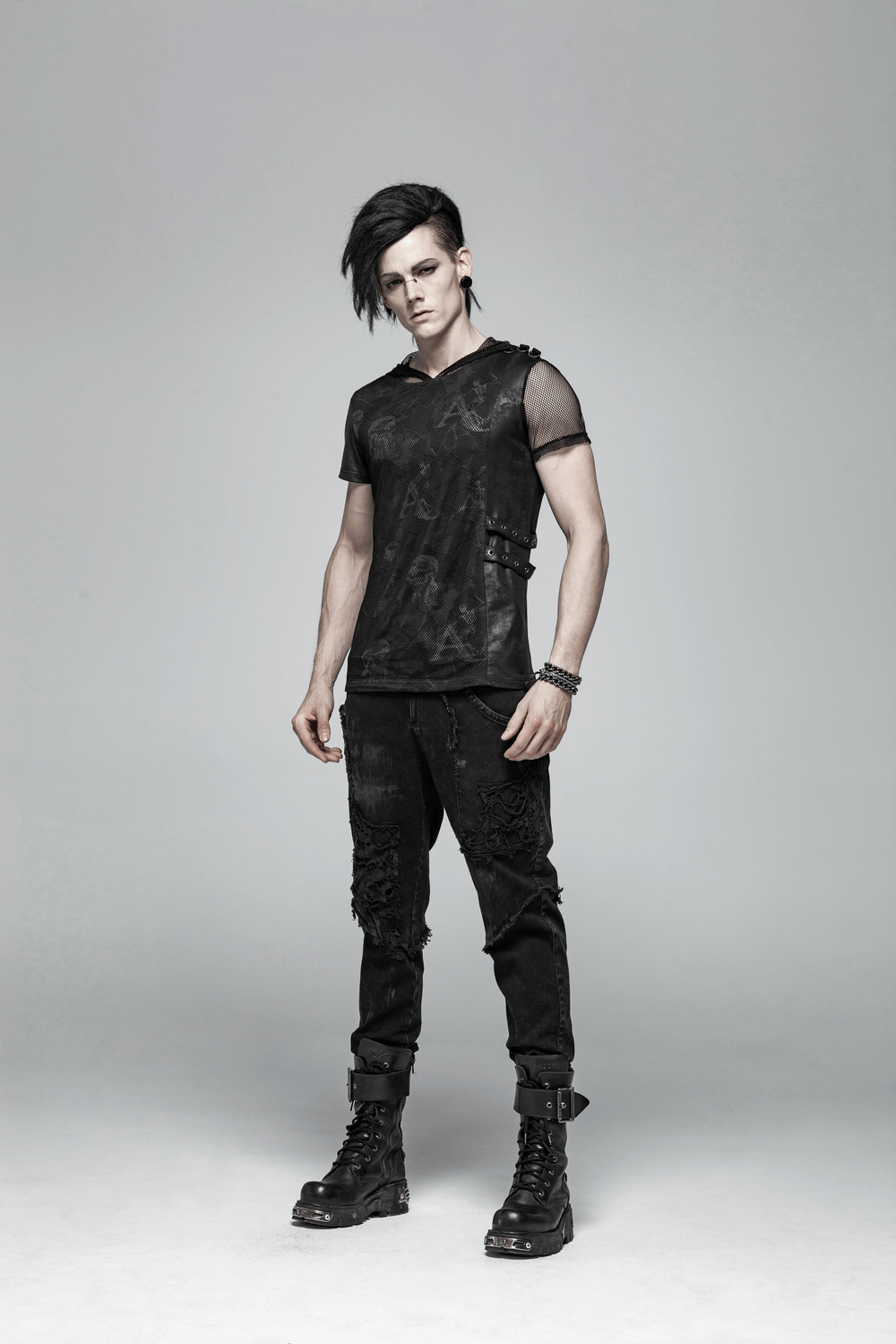 Stylish male model in black punk-style ripped jeans and a mesh top, showcasing urban streetwear fashion.