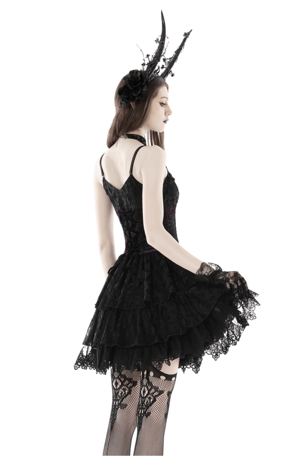 Model wears a black gothic mini dress with layers of lace and a corset, styled with horned headpiece and lace stockings.