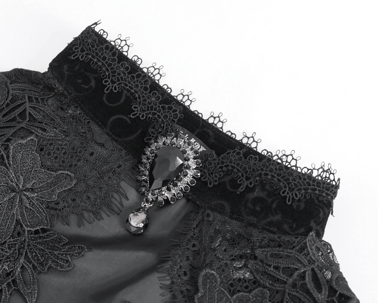 Close-up of elegant black lace fabric with intricate embroidery and a stunning gemstone detail for a gothic chic vibe.
