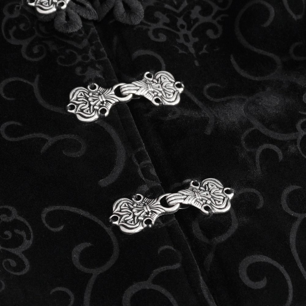 Close-up of ornate silver clasps on a black velvet fabric, showcasing intricate detailing and gothic elegance.