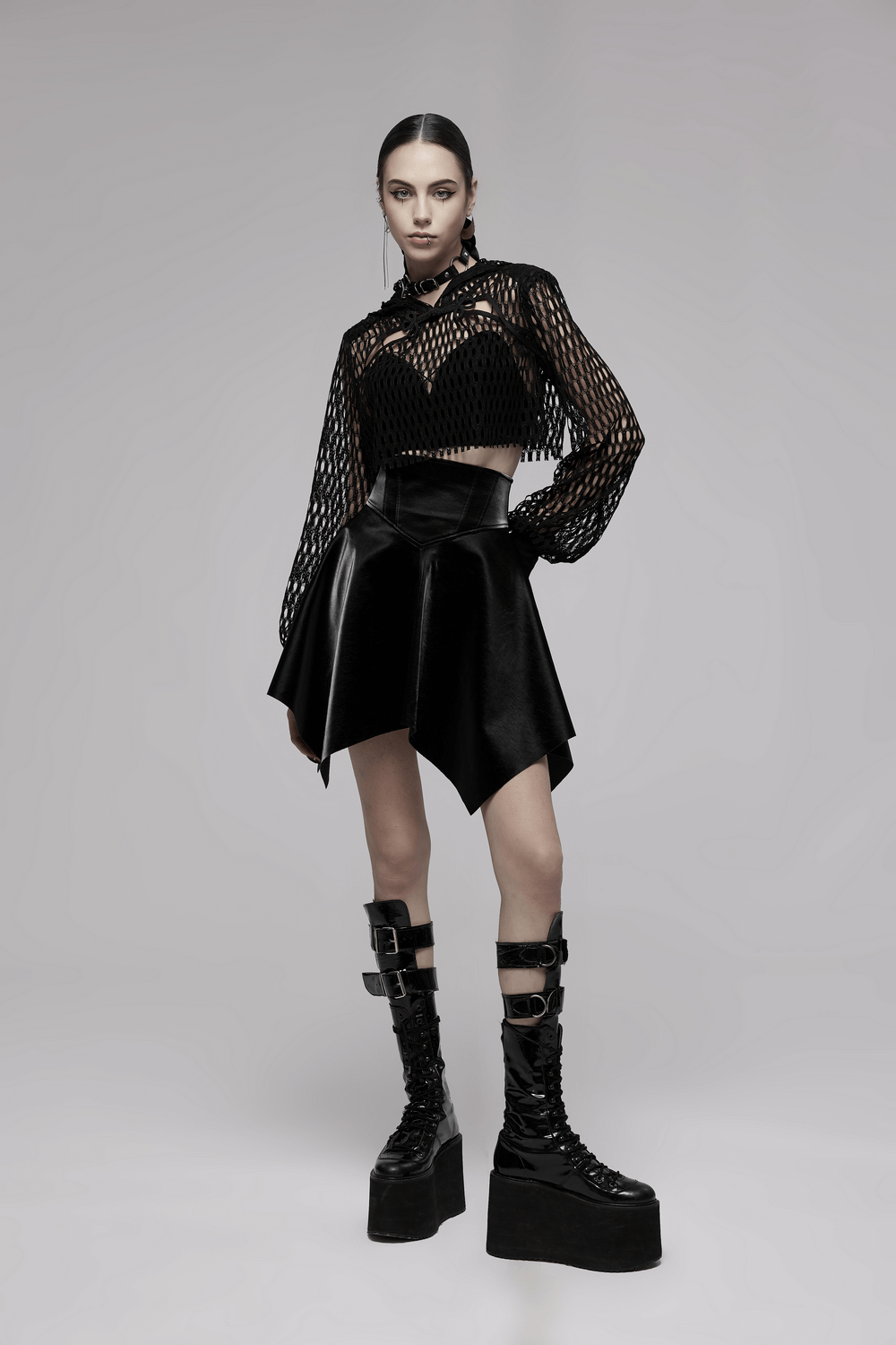 Trendy model in a black sheer mesh crop top hoodie and edgy skirt, exuding punk rave vibes with bold platform boots.