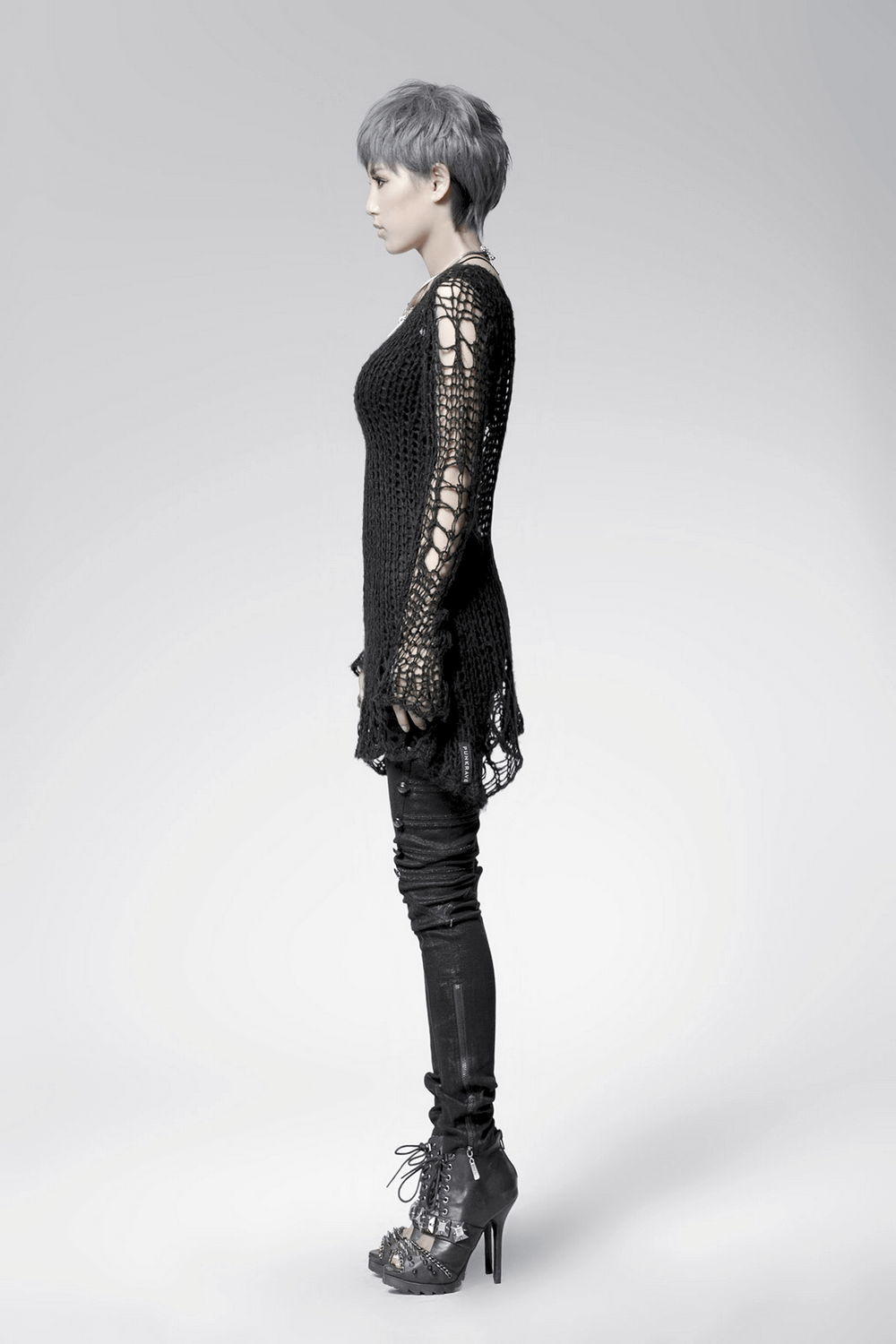 Model wearing a black shredded knit crocheted sweater with long sleeves, styled in a punk rave gothic fashion.