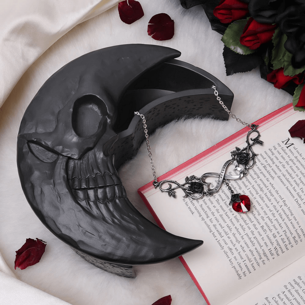 Black skull crescent moon jewelry storage box with lunar texture, adorned with a gothic necklace and red roses.