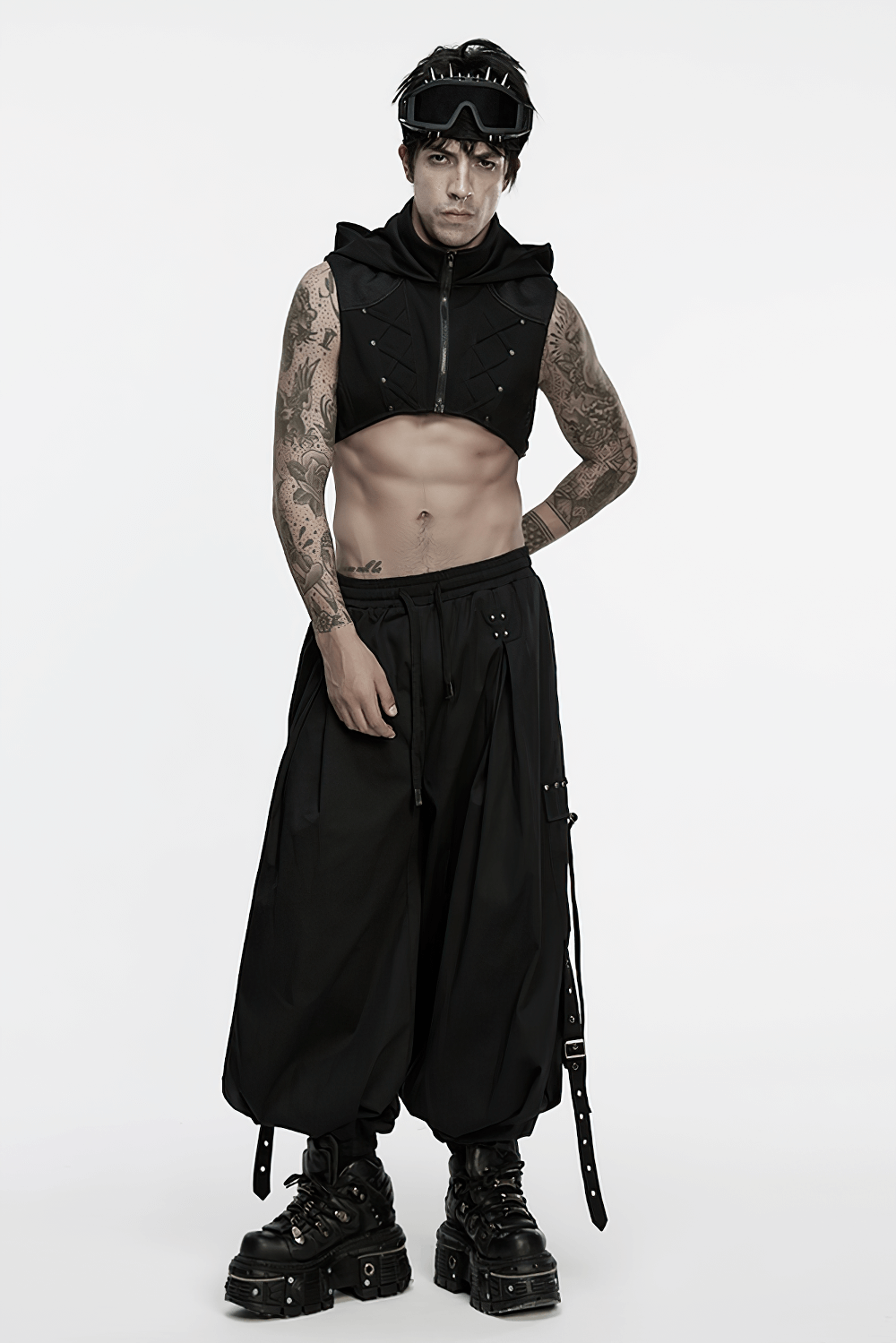 model in punk fashion with sleeveless top, baggy pants, and goggles, showcasing edgy style and tattoos