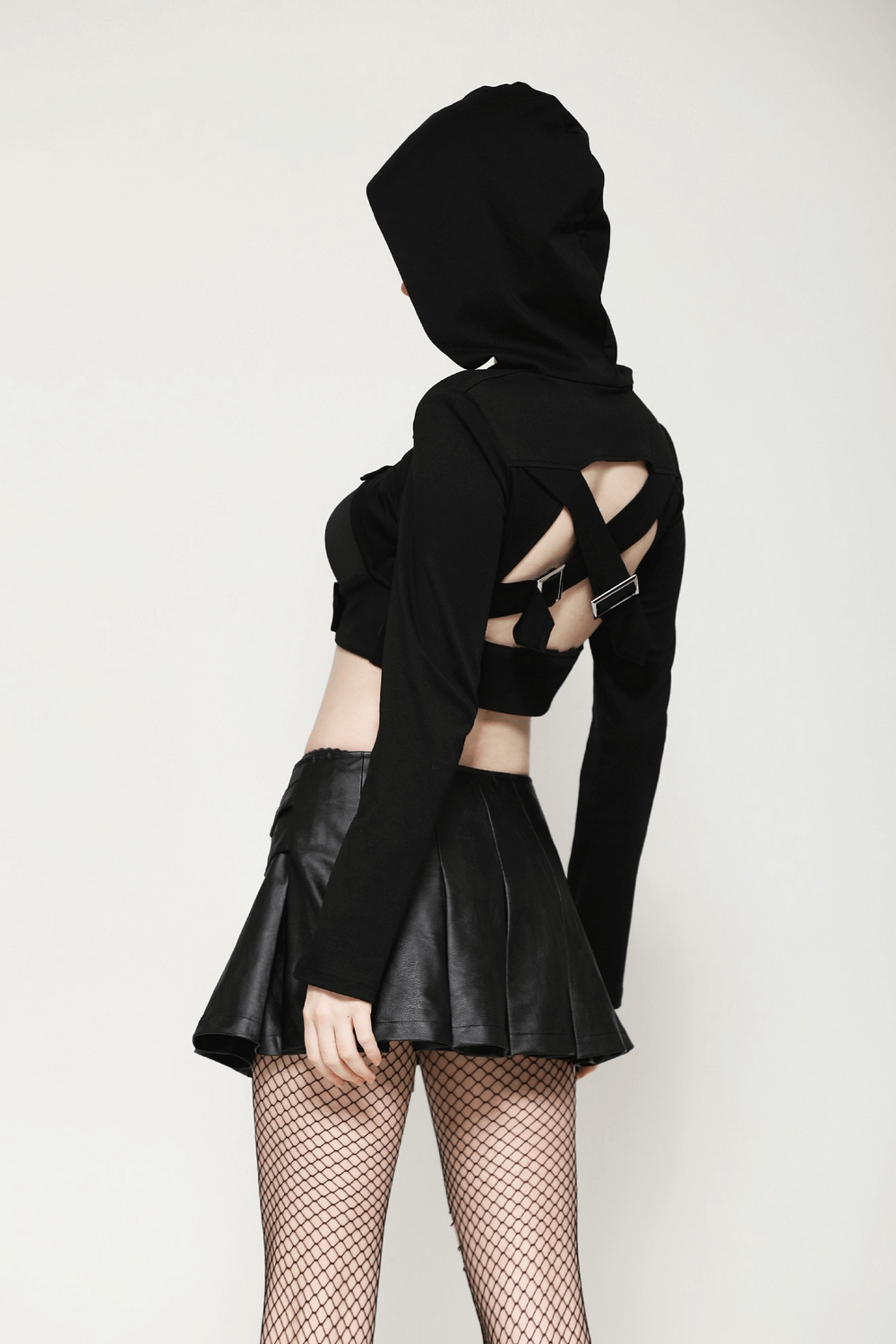 Black strappy hooded crop top with buckle accents and cutouts, paired with a leather skirt and fishnet tights.