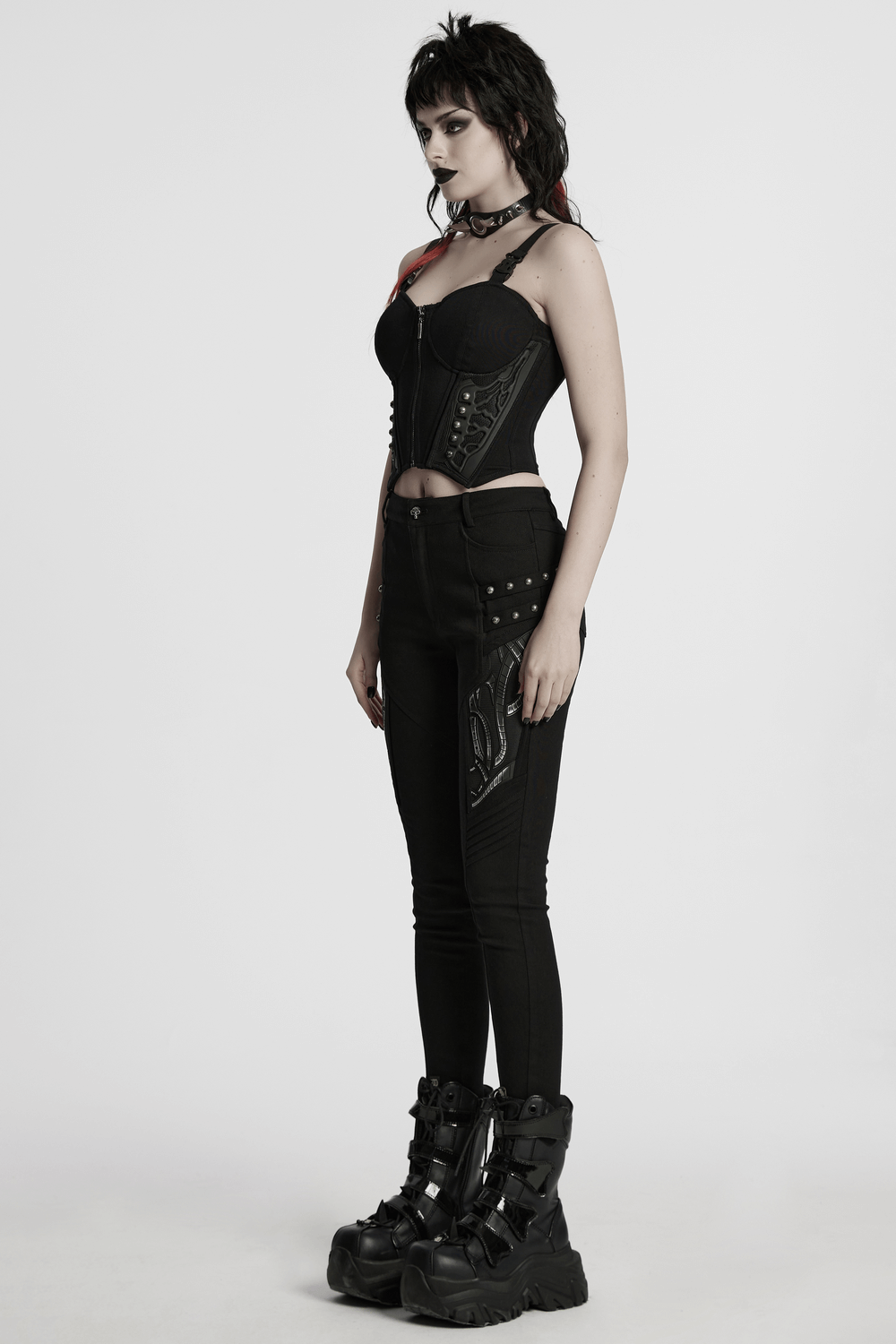 Model showcasing black techwear trousers with rubber patch details, paired with an edgy corset top and chunky boots.