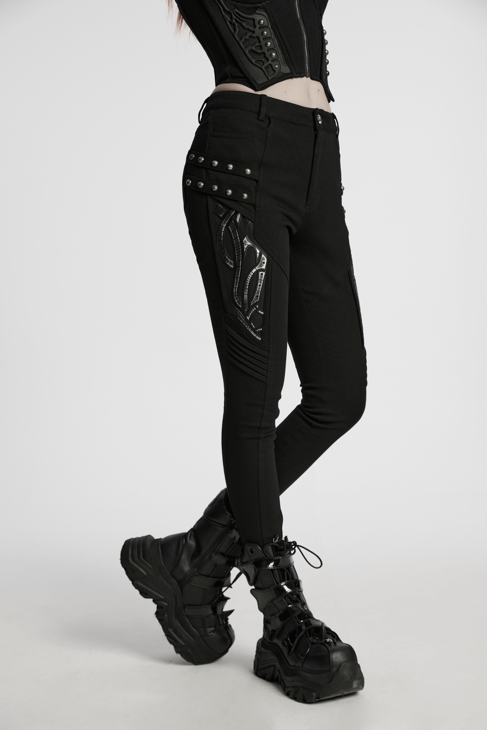 Black techwear trousers featuring rubber patch details, styled with edgy footwear for a modern street look.