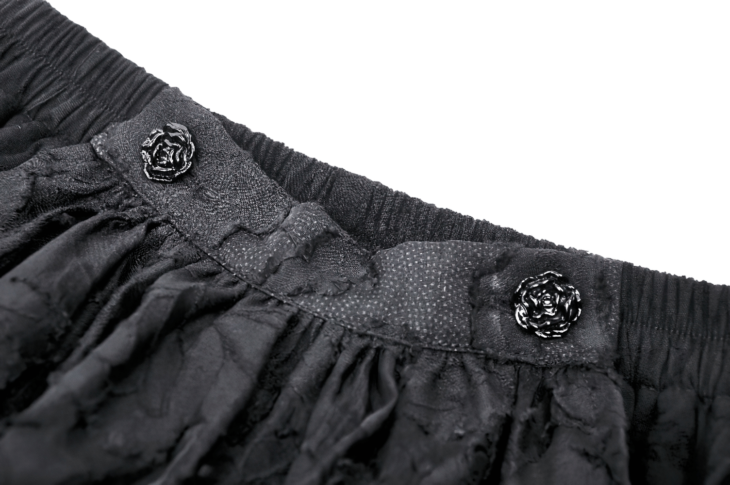 Close-up of black tiered ruffle skirt waistband with elastic and decorative flower buttons.