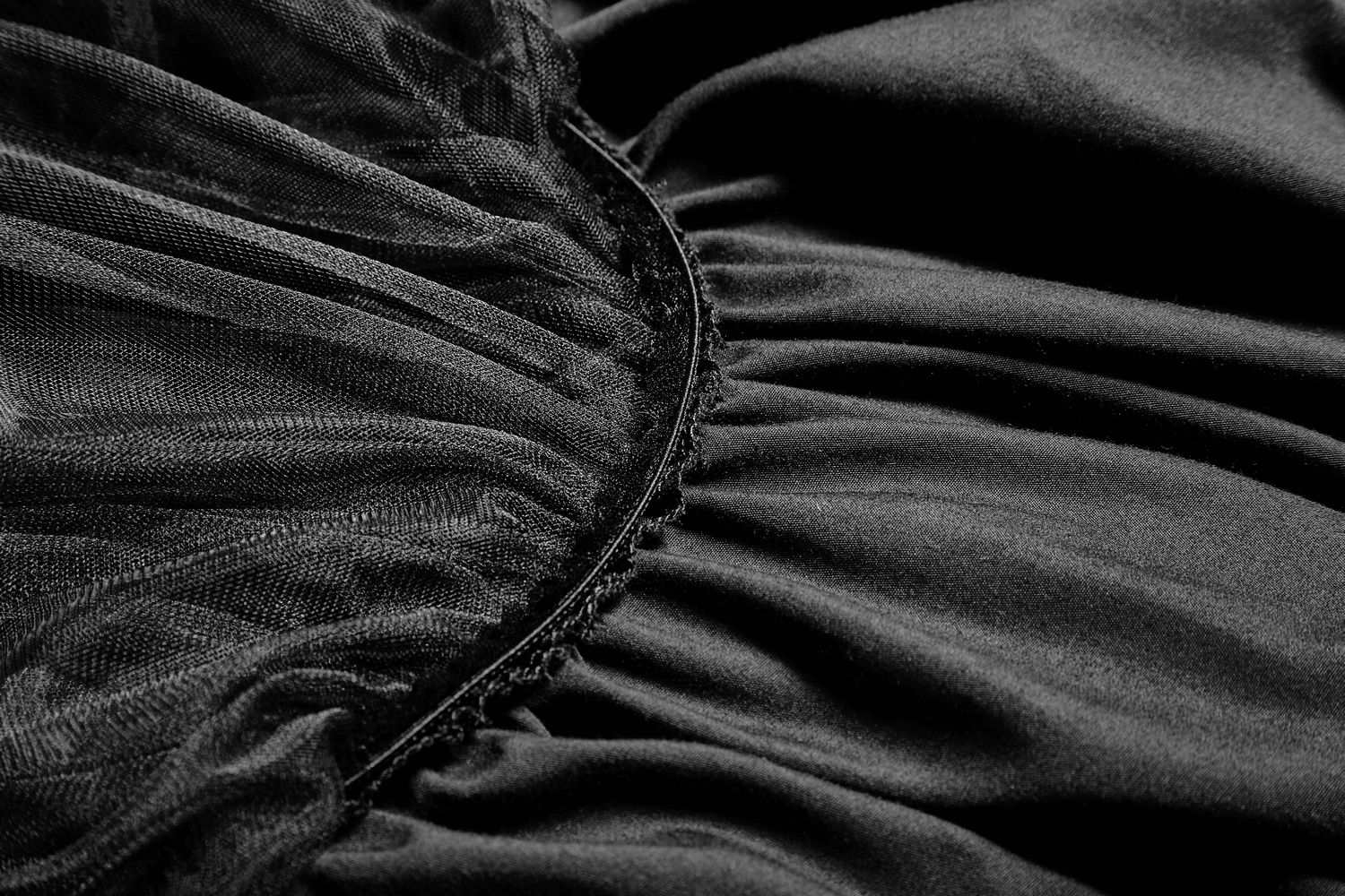 Close-up of black tulle fabric detail on a long skirt with lace trim, highlighting its soft mesh texture and pleated design.