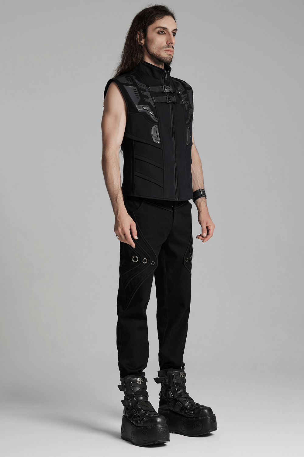 Model showcasing black sleeveless vest with straps, paired with black twill denim pants featuring eyelets and bold boots.