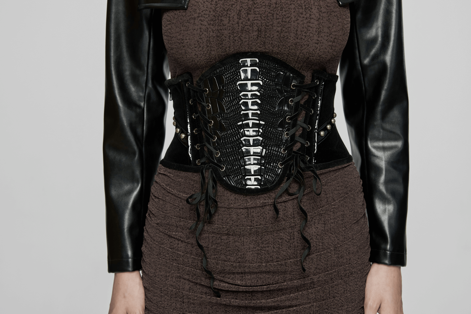 Black velvet and patent leather gothic corset belt with rivets and lace-up back, accentuating a curvy silhouette.