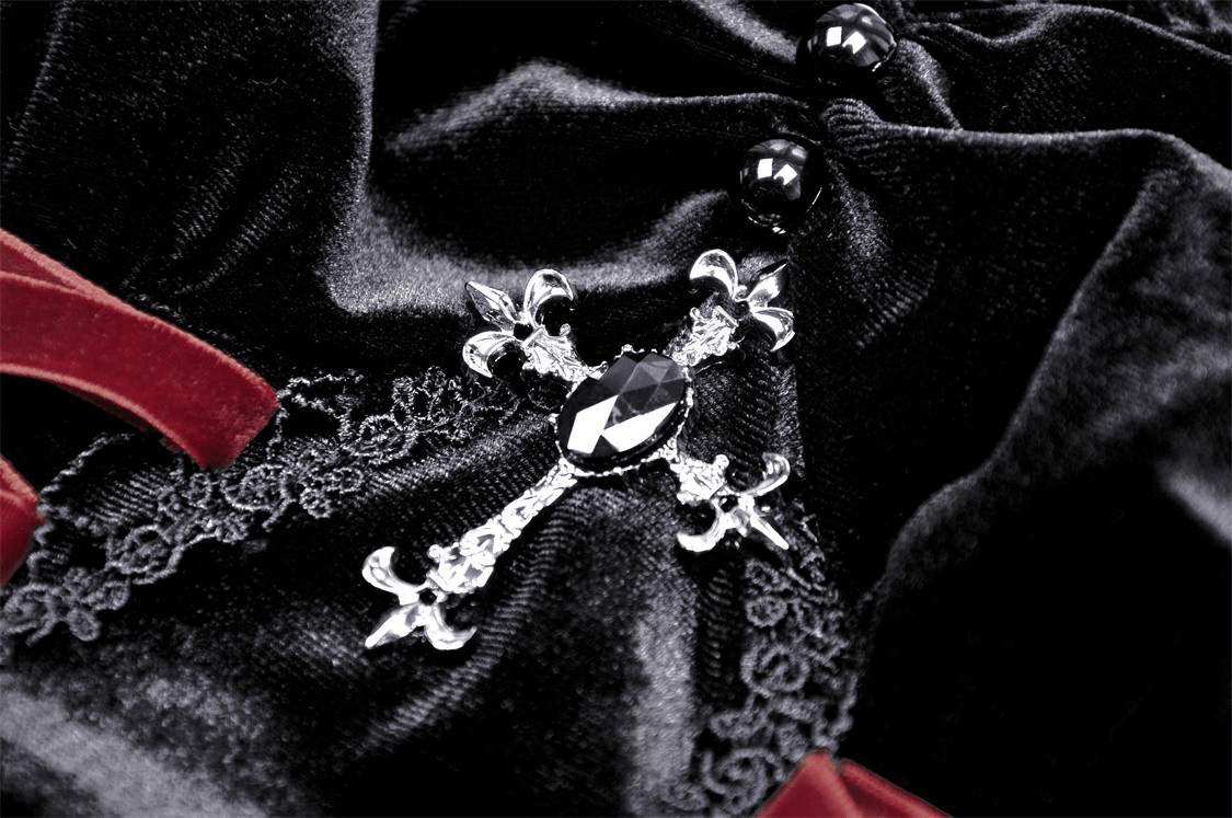 Close-up of a black velvet fabric featuring an ornate silver cross detail with a gem, perfect for gothic fashion.
