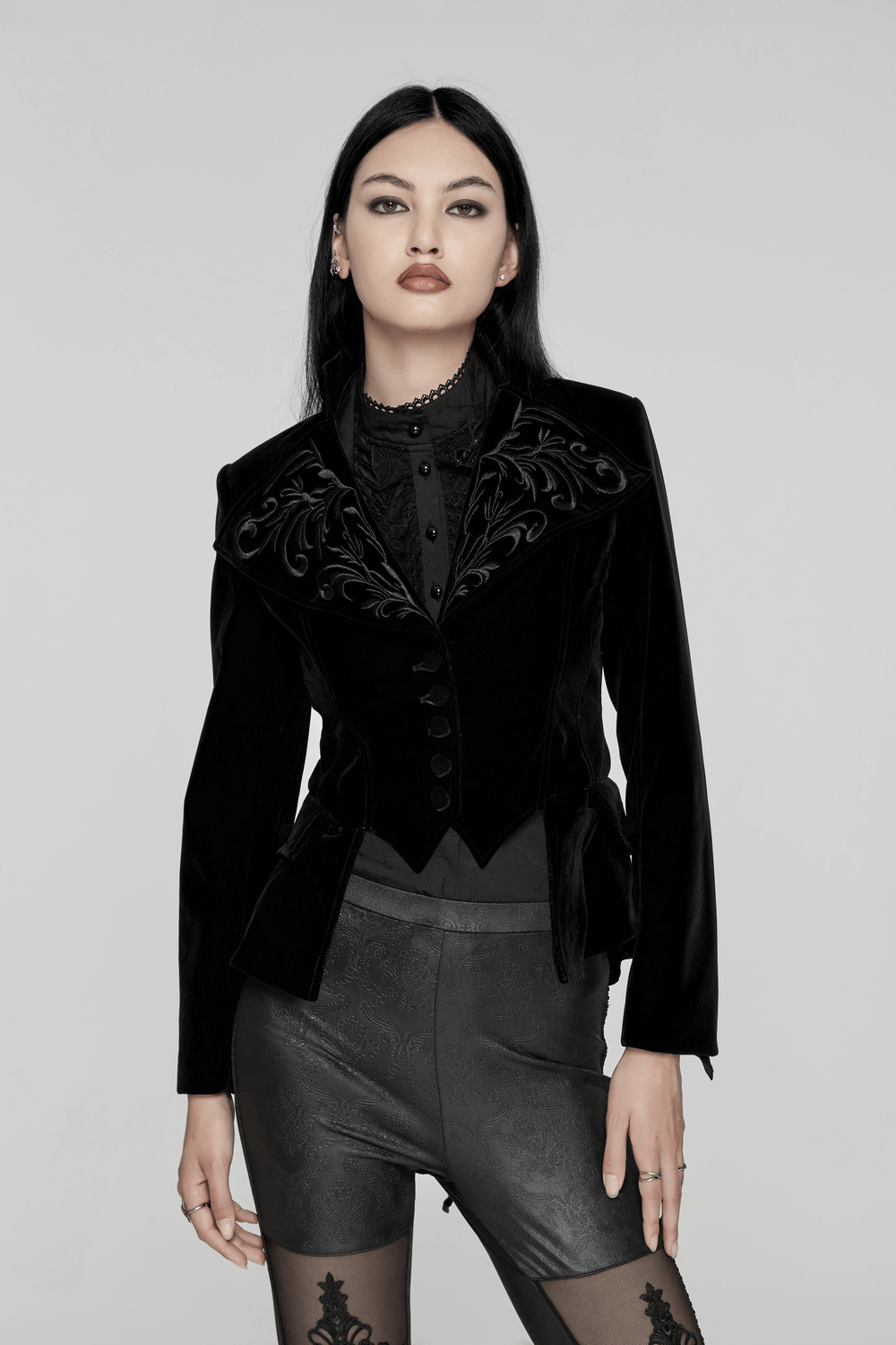 Black velvet Gothic tailcoat with embroidered collar and corset waist detail, featuring textured buttons and pleated pocket covers.