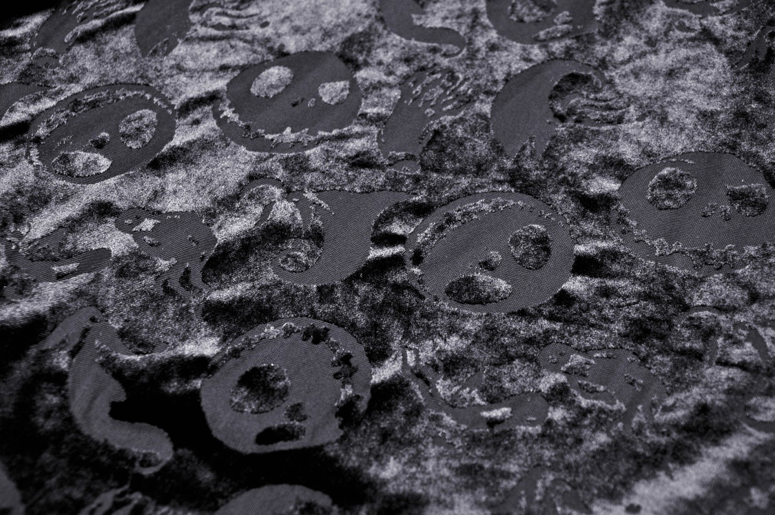 Close-up of black velvet fabric featuring skull print design, perfect for gothic Halloween capes and cosplay.