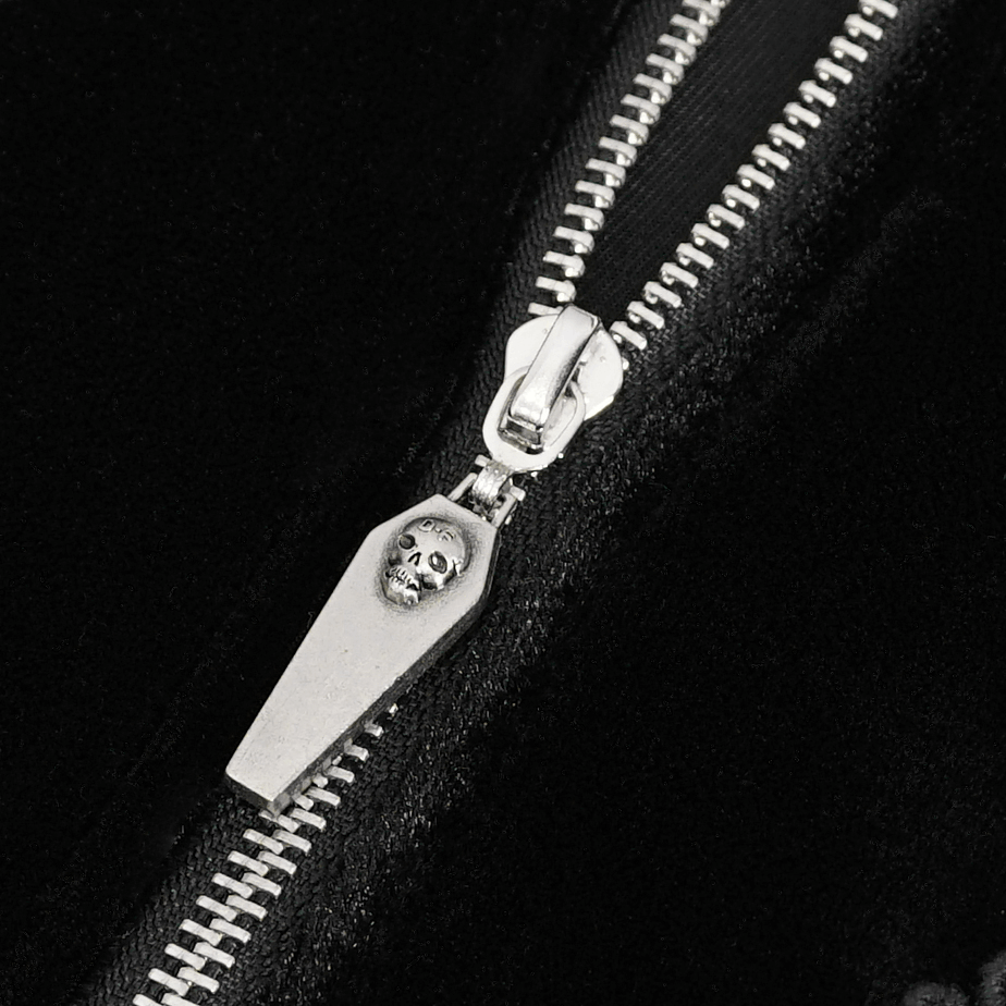 Close-up of a black velvet zipper with a unique skull coffin pull, adding edgy detail to a stylish bodysuit.