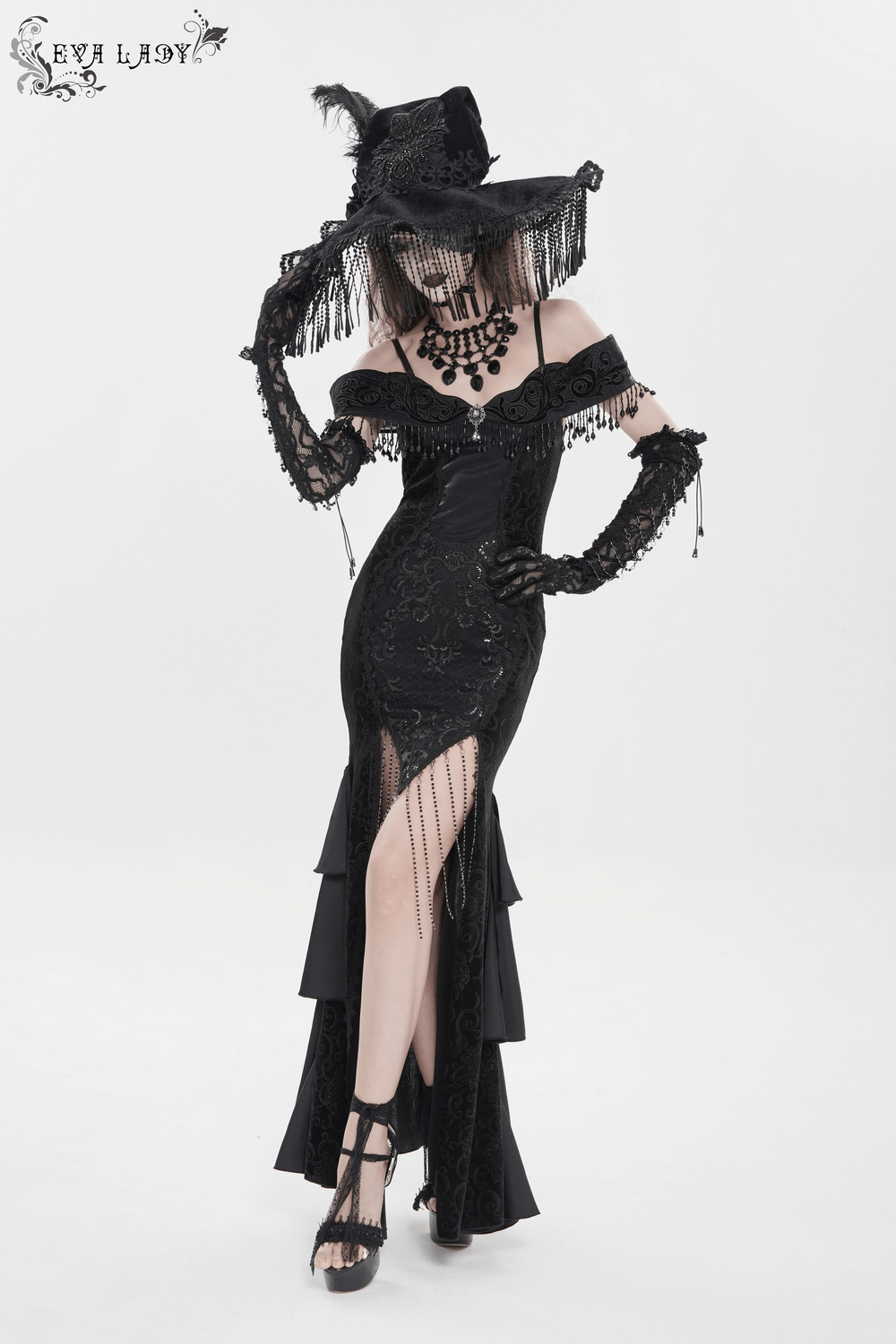 Black Witch Hat with Lace Fringe and Feather Detail worn with a gothic black dress, featuring intricate lace and a daring slit.