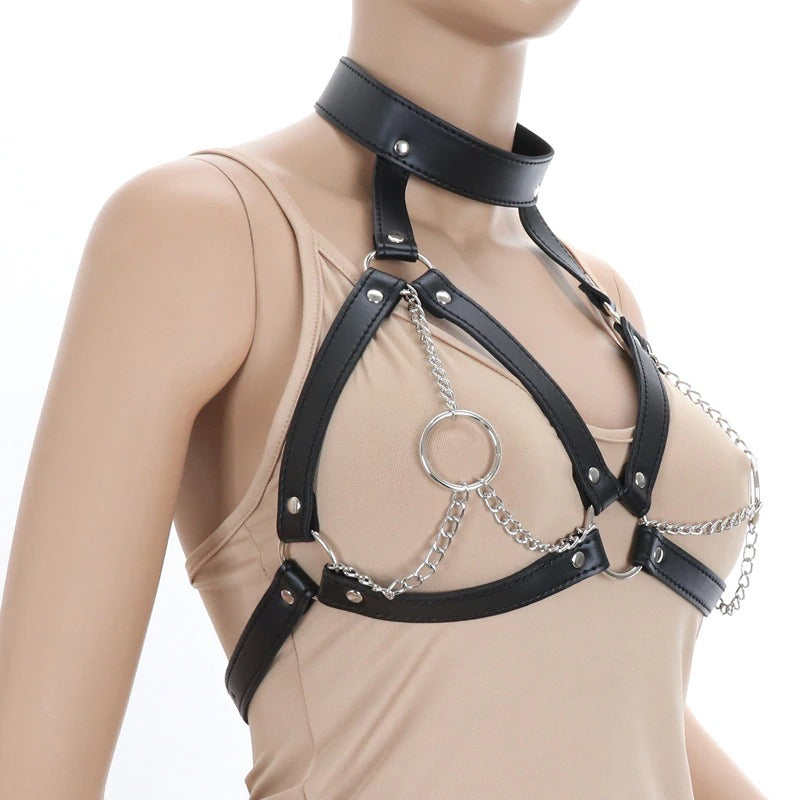 Faux leather breast bondage harness belt with iron chains and rings, styled over a beige top, offering a daring and gothic fashion statement.