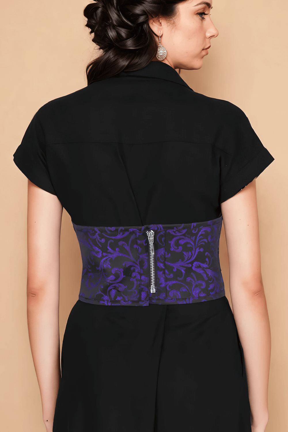 Rear view of a model showcasing a purple brocade corset-inspired belt with a zip closure, styled over a black outfit.