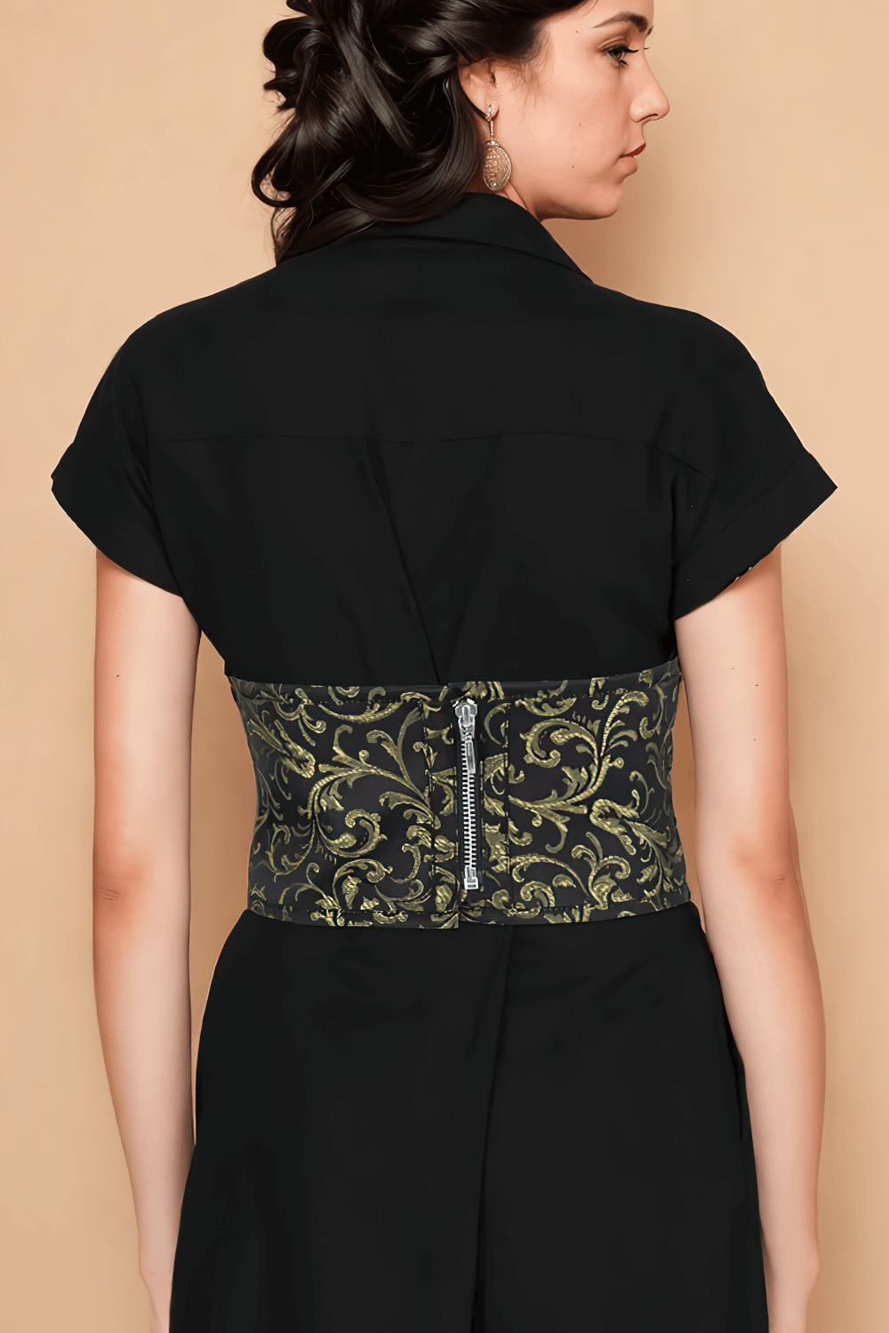 Back view of a woman wearing a black dress with a gold brocade corset belt, featuring lace-up details and a zip closure.